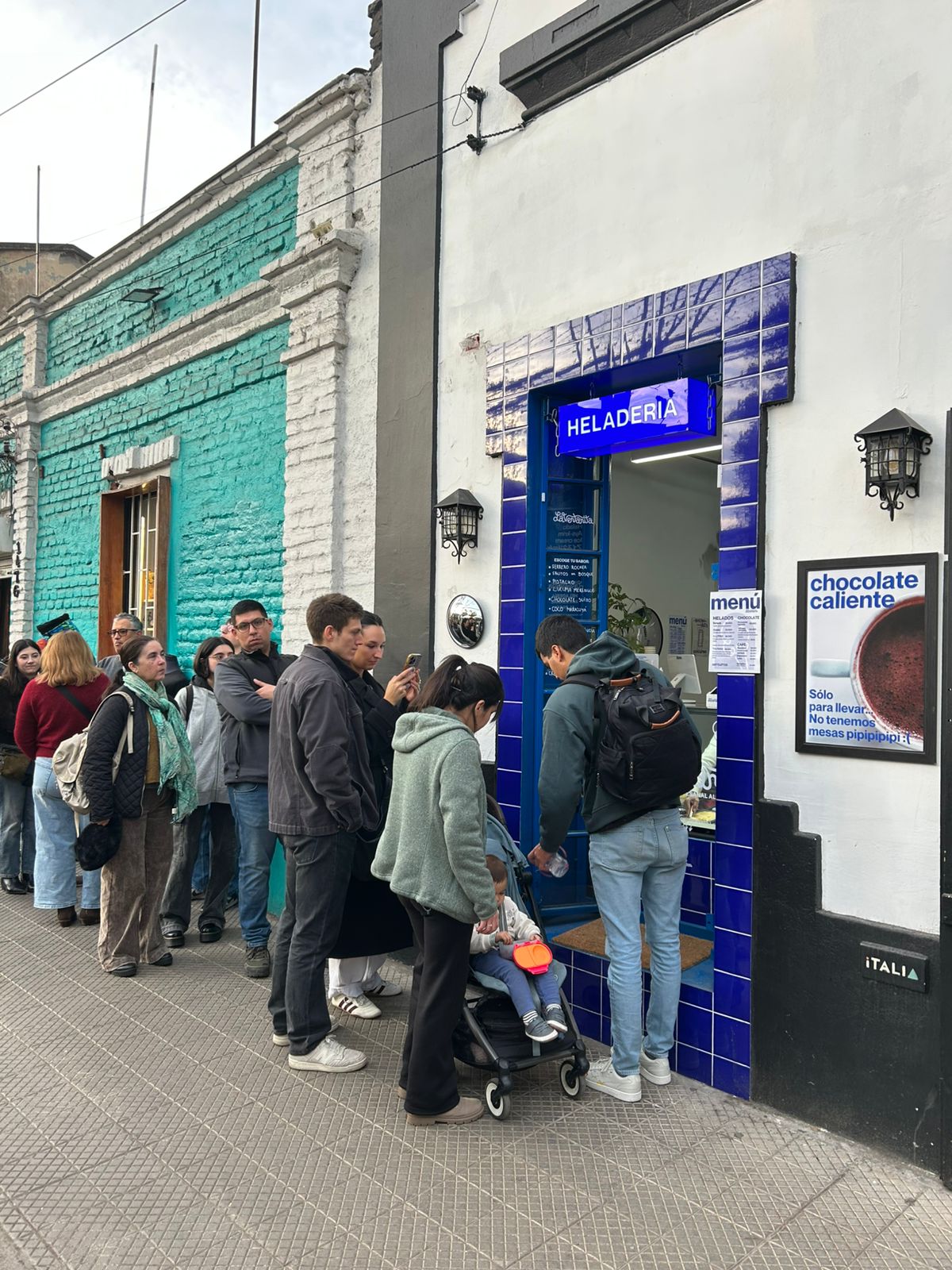 Fila de personas esperando afuera de La Ventanita en Barrio Italia durante el día
